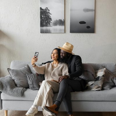 Full body of content Asian woman and African American man having video call while sitting on couch with crossed legs in room